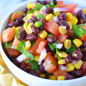 black bean and corn salsa recipe close up in a white bowl and chips around it