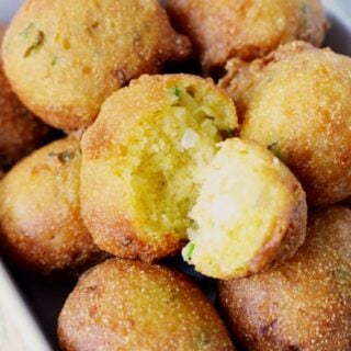 pile of hush puppies on a white plate with one split open showing a center.