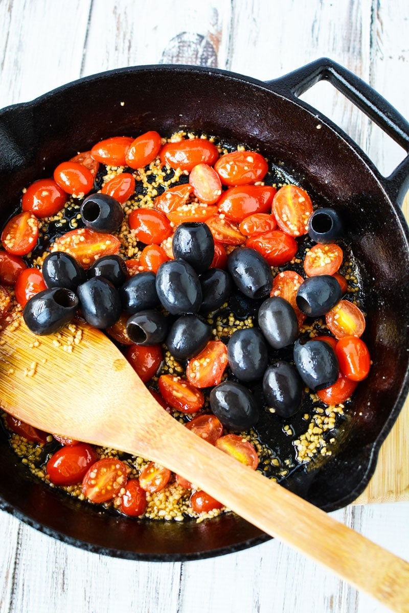 stirring tomatoes and olives with a wooden spoon.