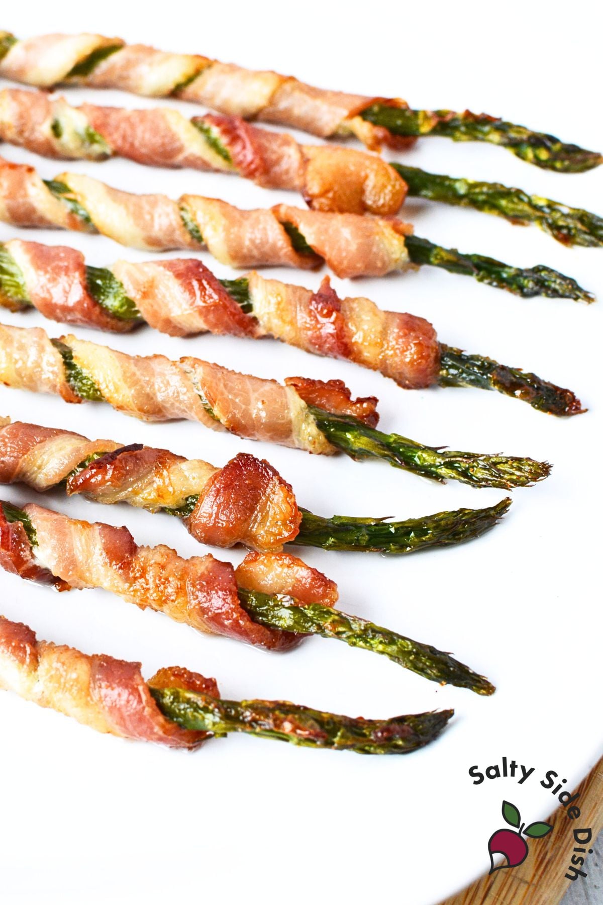 Crispy baked bacon wrapped asparagus with golden brown bacon on white serving plate