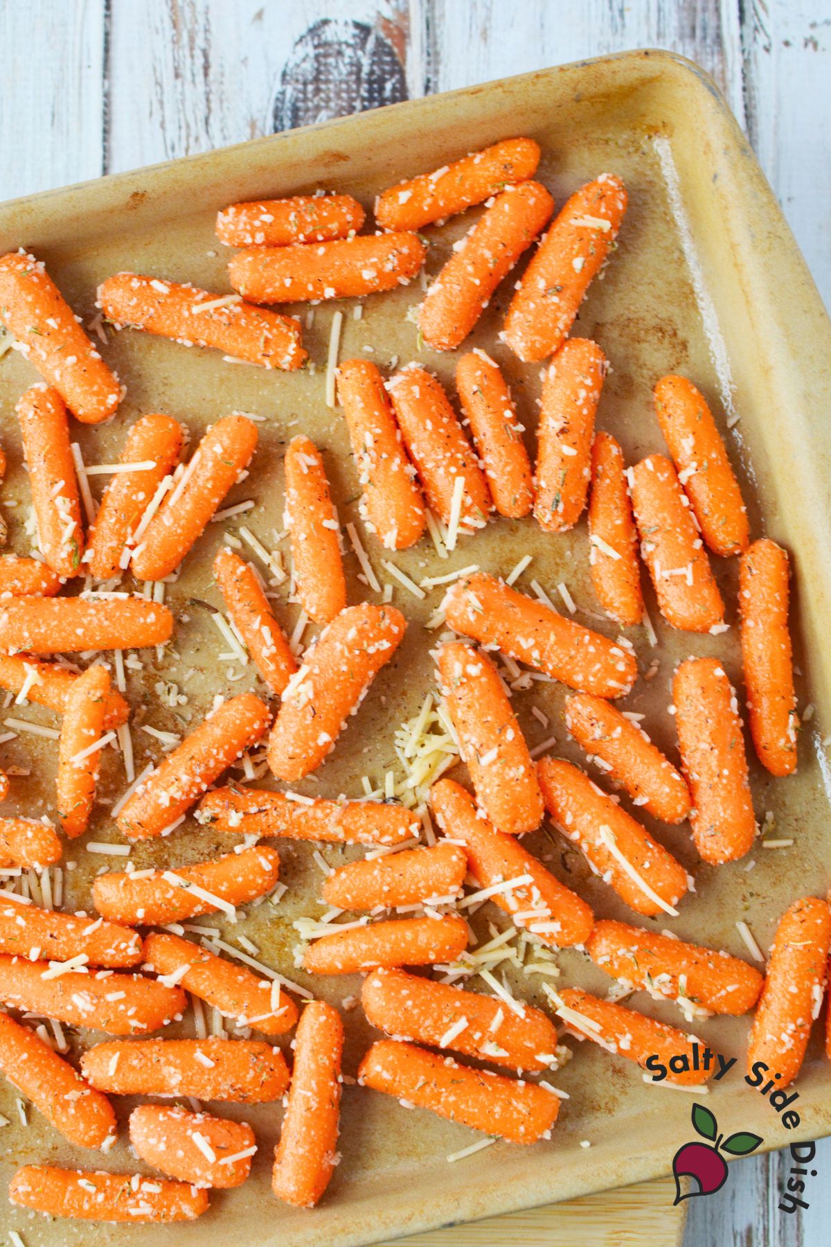 seasoned baby carrots with parmesan cheese spread on a baking sheet before roasting
