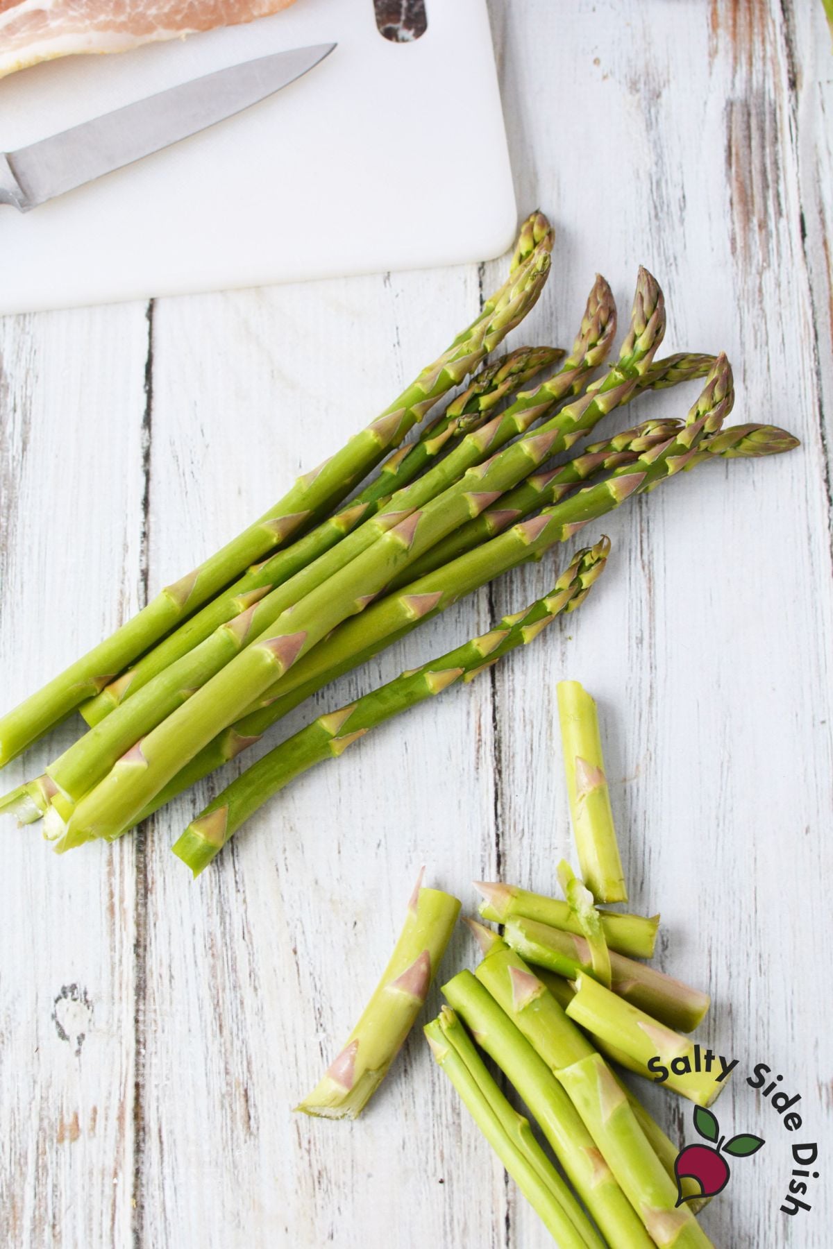 Trimmed asparagus spears on white cutting board showing woody ends removed