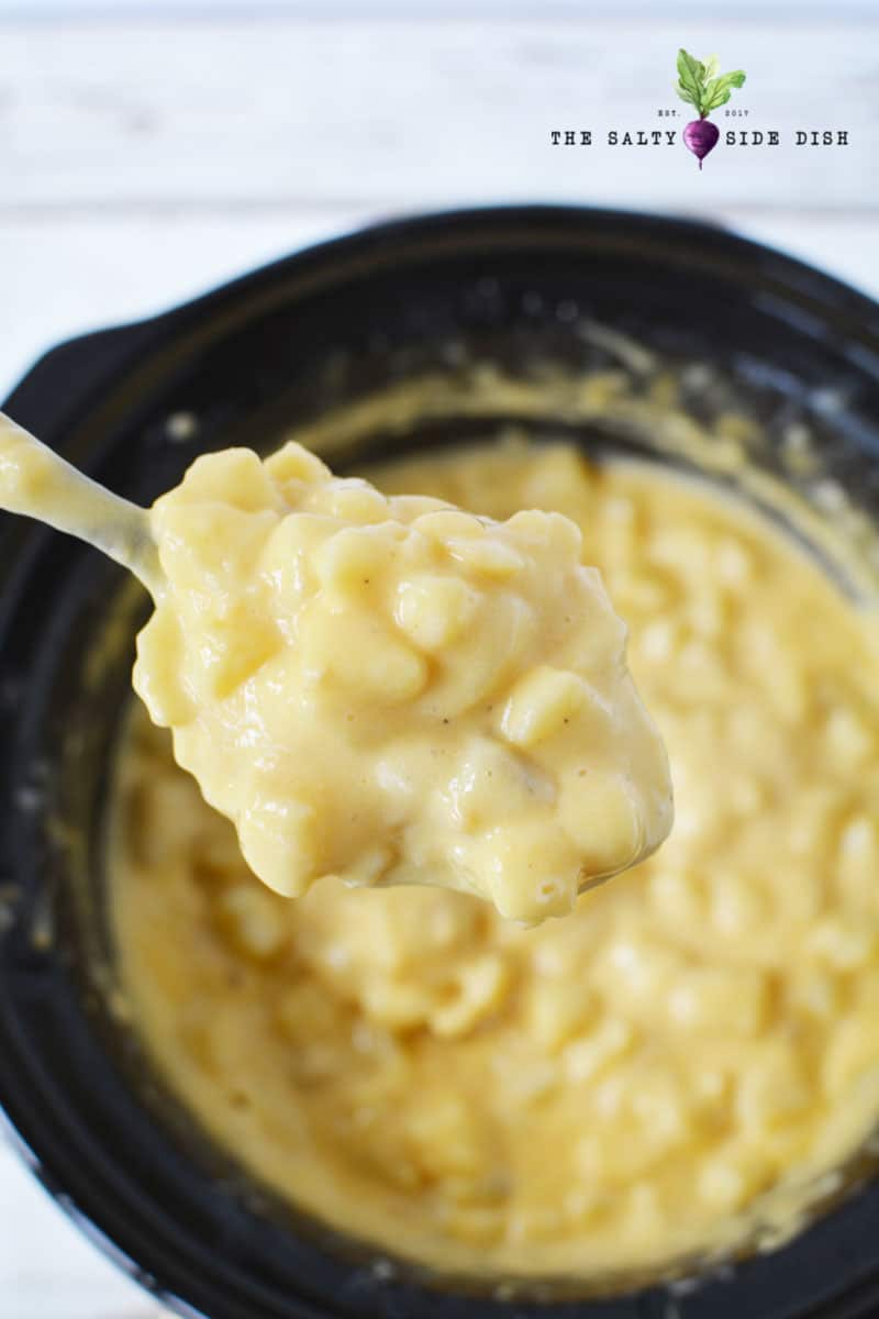 cheesy potatoes in a crockpot being lifted by a spoon ready to serve for a holiday meal
