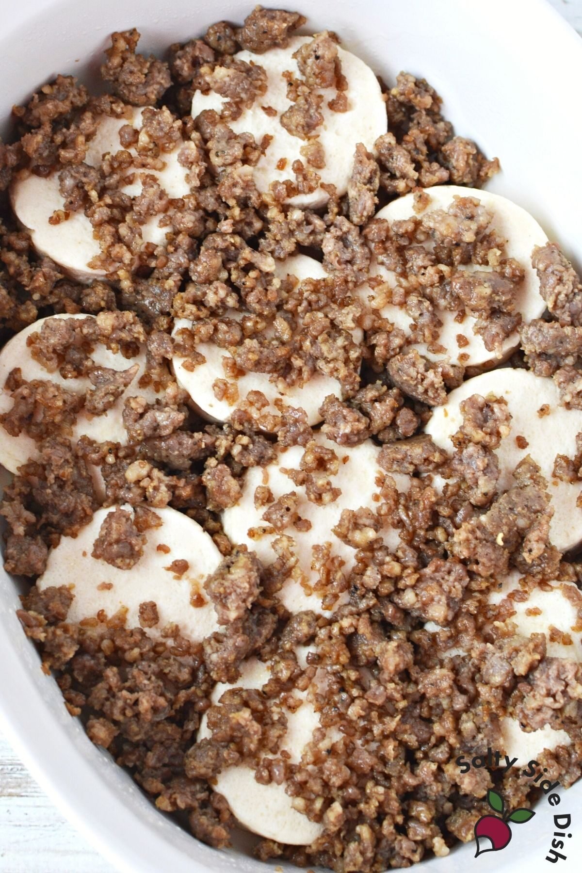 layered breakfast sausage over dense rolls in a casserole dish.