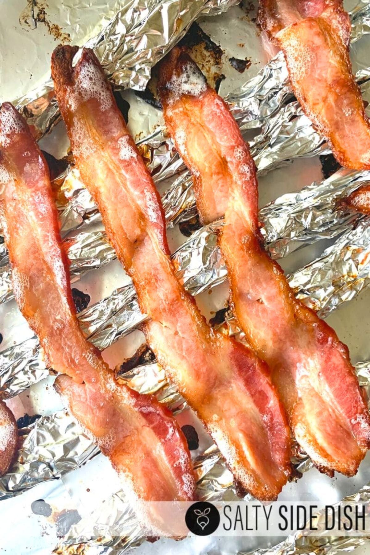 cooked bacon strips placed on foil rack ready to bake in the oven