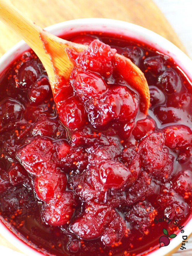 cranberry sauce in a bowl with a wooden spoon stirring sauce
