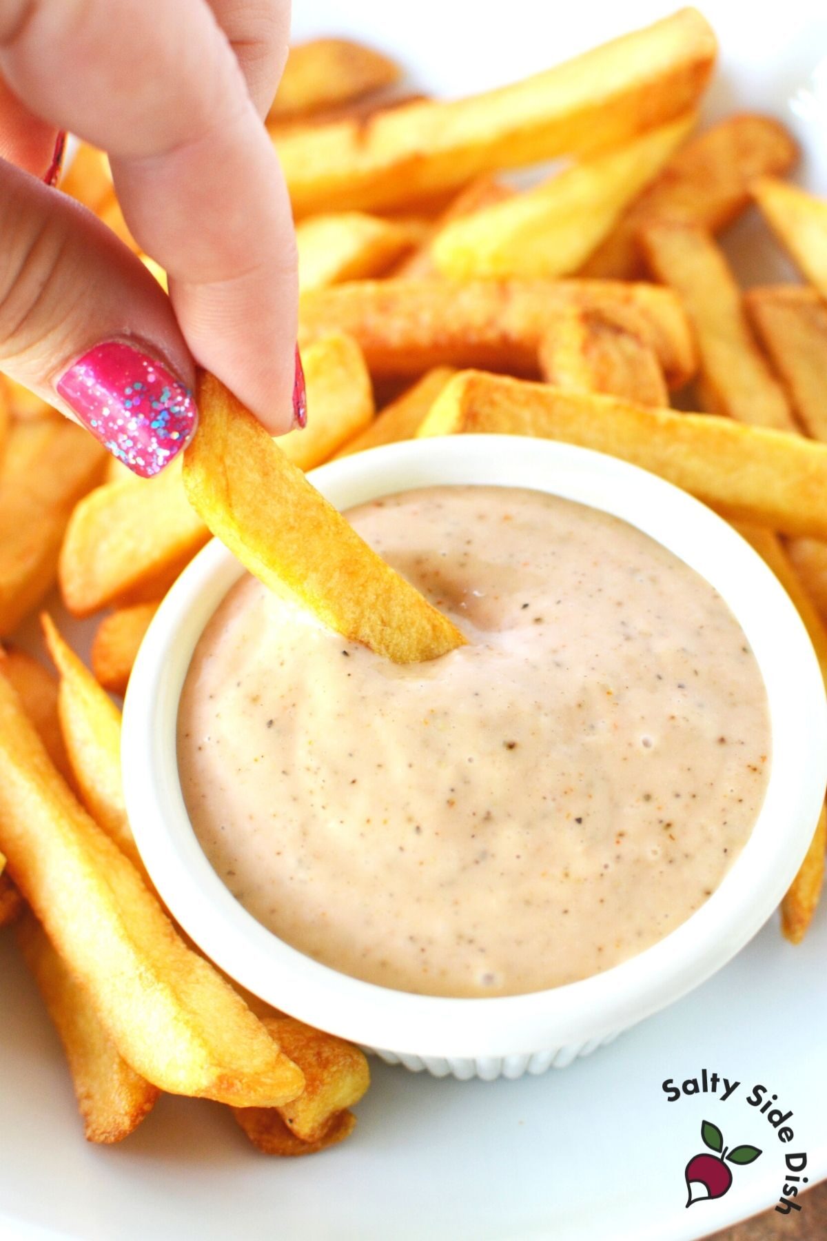dipping a French fry into a bowl of sauce.