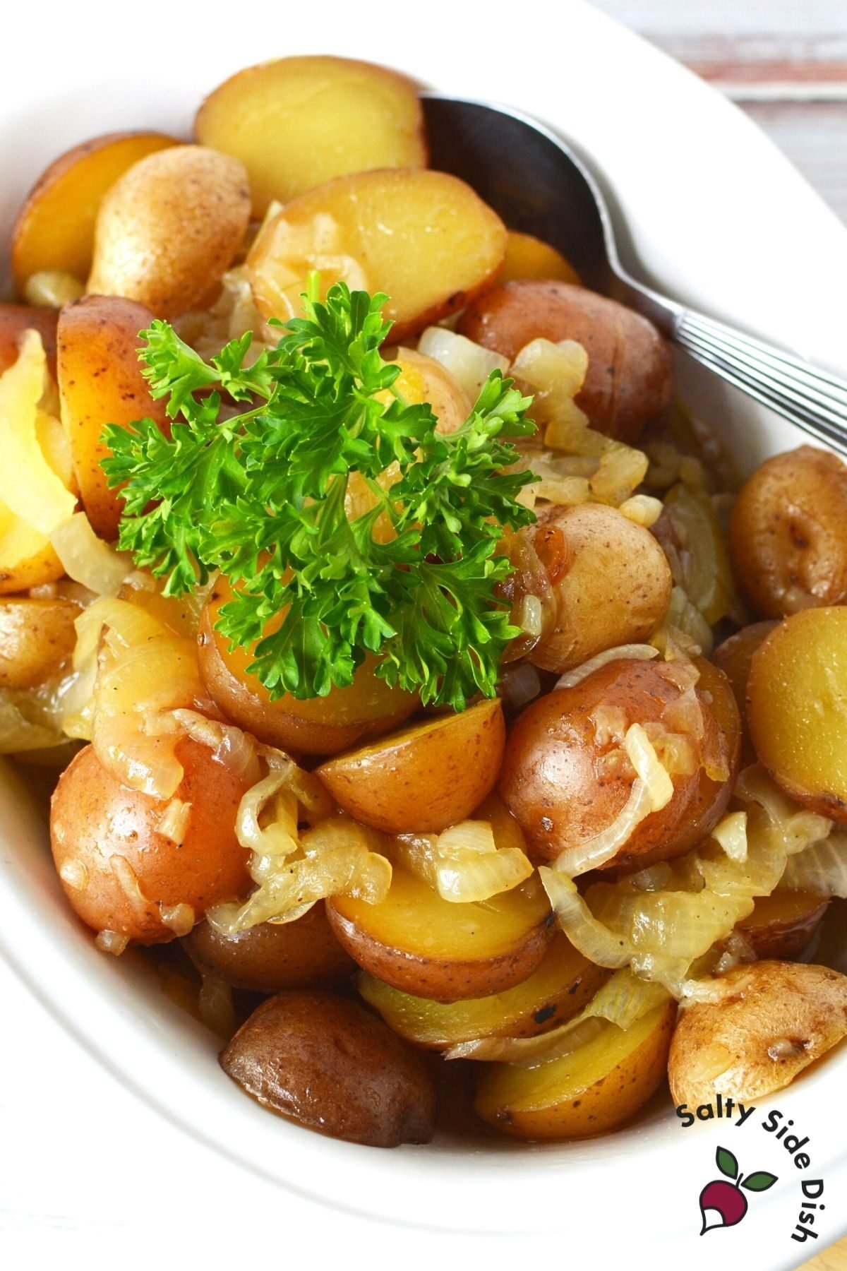 cooked red potatoes and onions in a white bowl with a sprig of parsley on top.