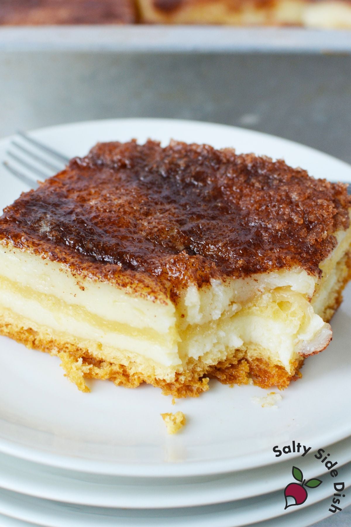 Slice of sopapilla cheesecake bar on a plate showing the cream cheese filling and crescent roll layers