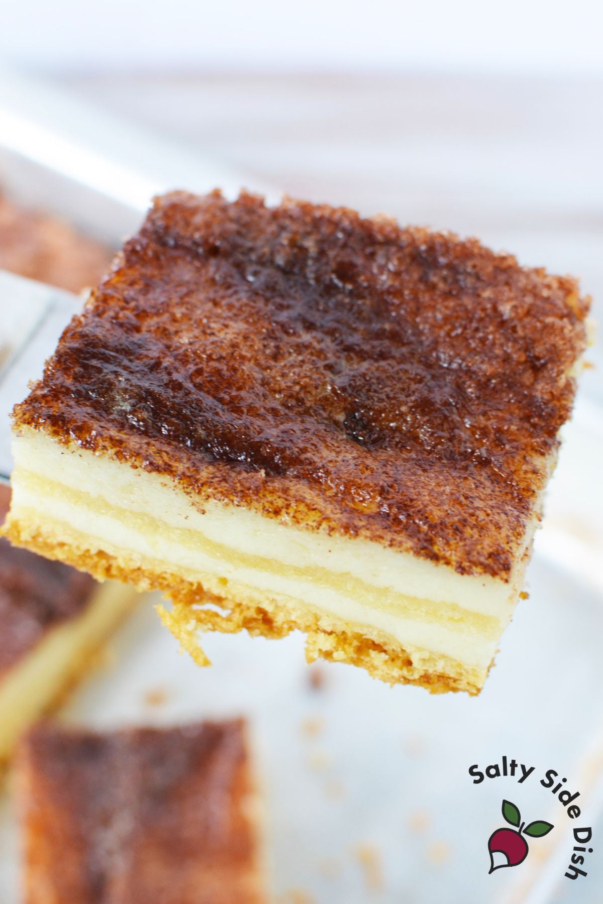 Close up of a sopapilla cheesecake bar lifted on a spatula showing the cinnamon sugar crust and creamy filling