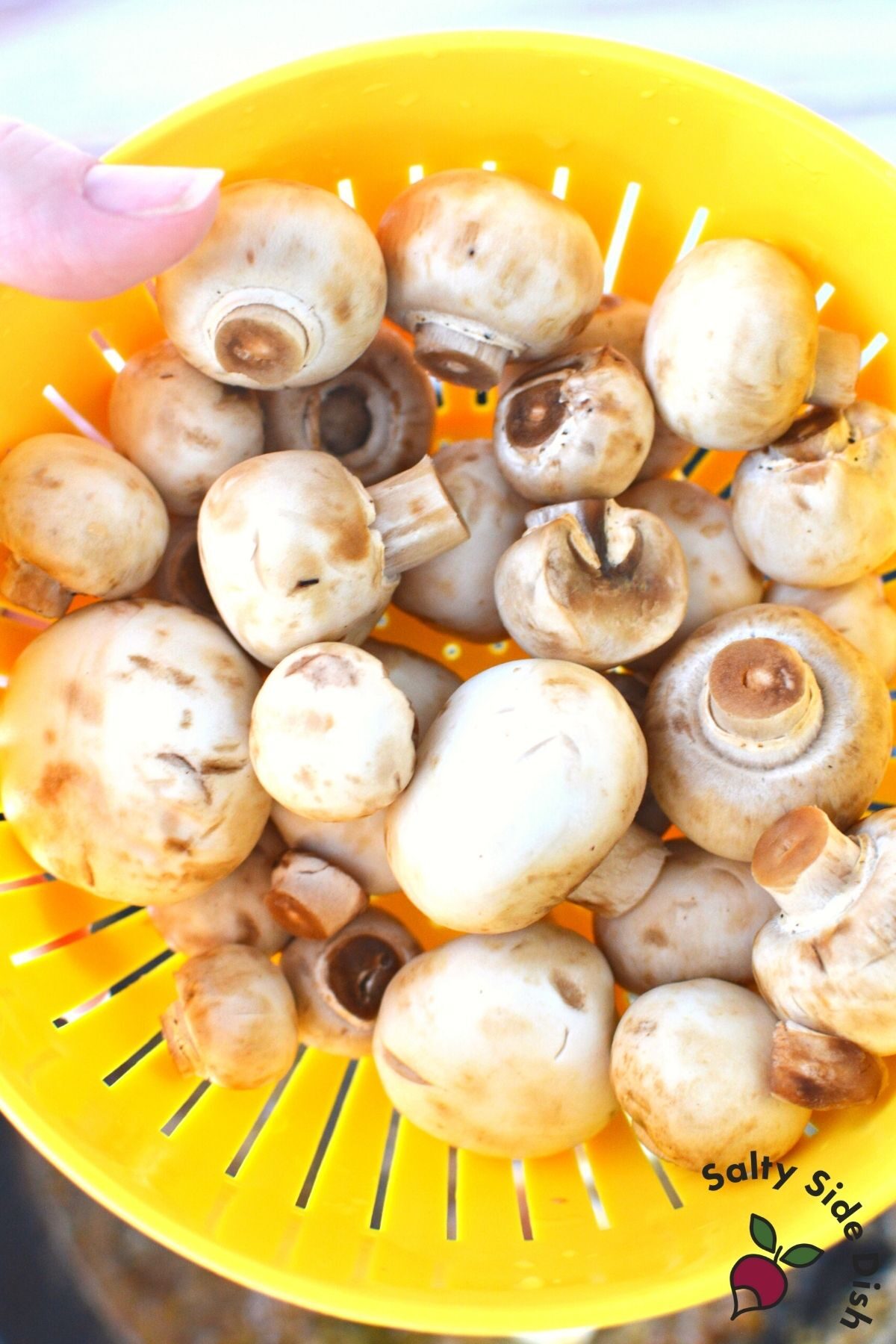 white button mushrooms in a yellow colander freshly rinsed.