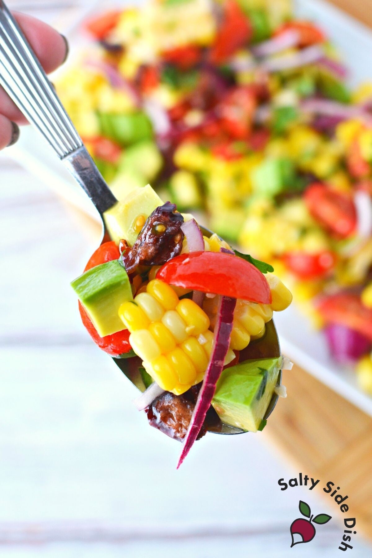 spoonful of corn salad with tomatoes, red onions and avocado.