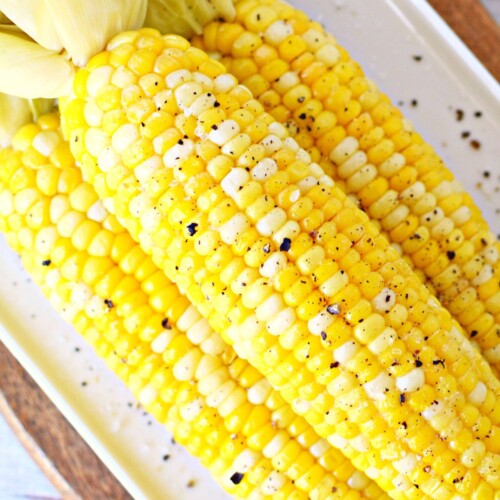 Closeup of 3 ears of boiled corn on the cob on a plate sprinkled with pepper.