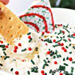 graham cracker being dipped in christmas cake dessert dip.
