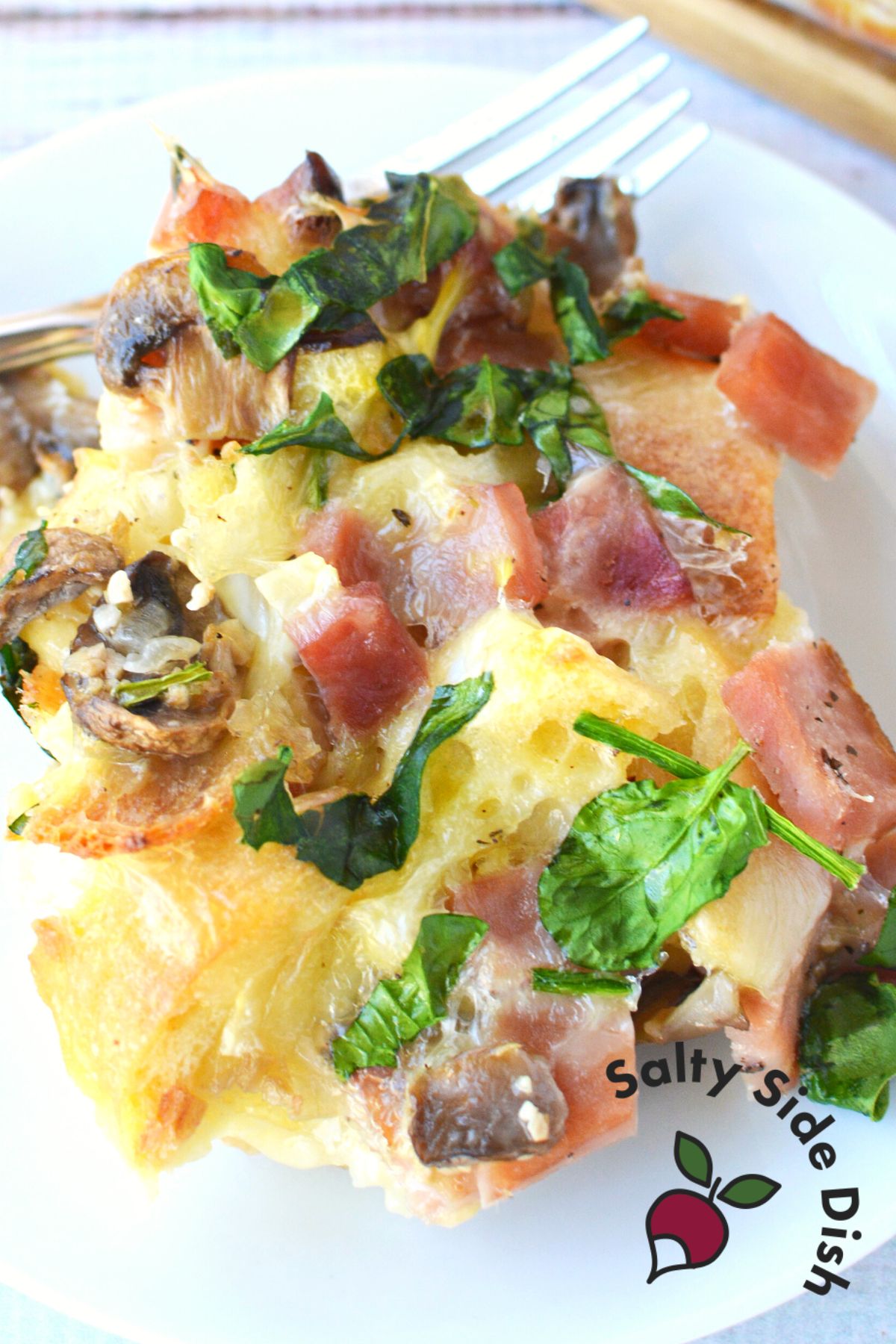 cooked strata on a white plate with fork in background.
