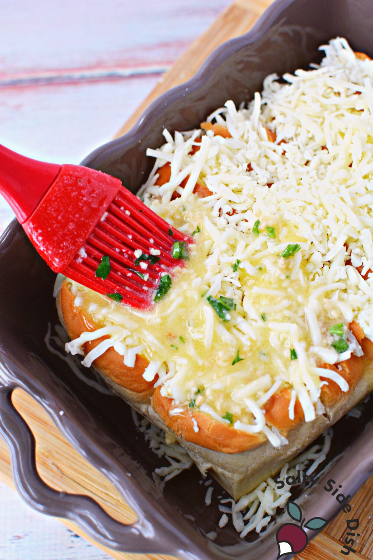 adding flavored butter to top of Hawaiian rolls.
