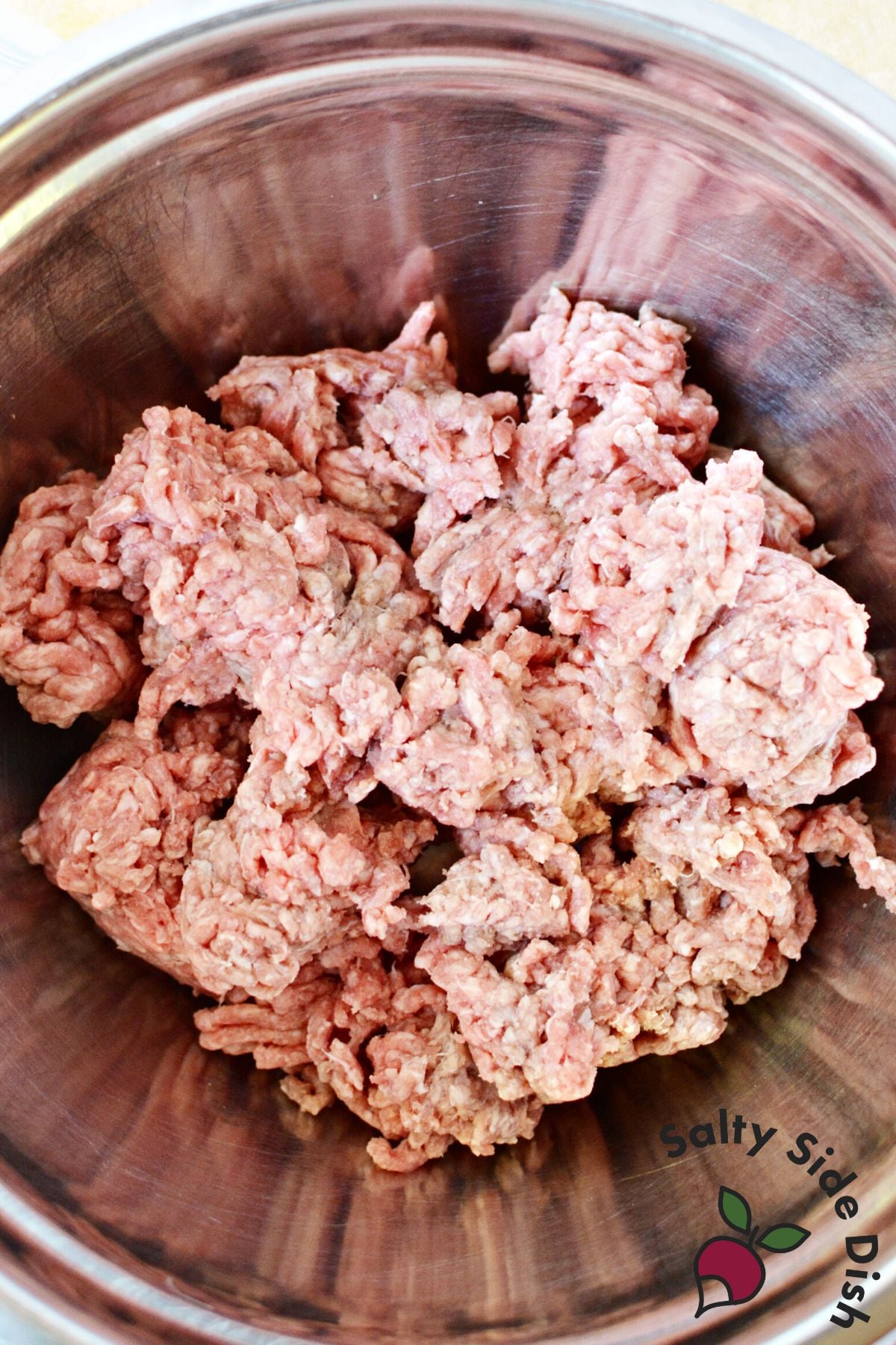 ground beef with seasonings in a silver mixing bowl.