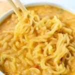 ramen noodles in a white bowl being stirred by chopsticks.