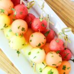 melon ball fruit skewers on a white serving platter.