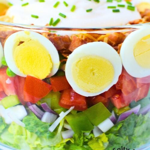 Layered salad in a glass trifle bowl with colorful vegetables.
