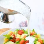 homemade dressing in a boat being poured over a salad.