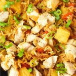 Overhead view of chicken and pineapple fried rice in a skillet, garnished with sliced green onions and pineapple chunks.