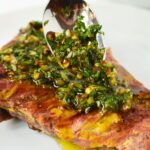 Homemade Chimichurri Sauce in a spoon being spread on a steak.