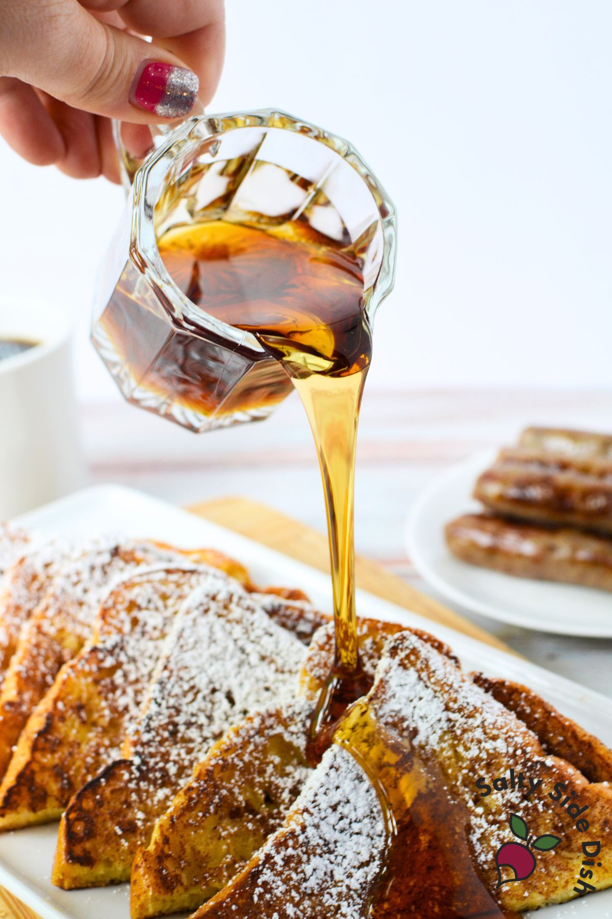 Pouring maple syrup over brioche French toast dusted with powdered sugar for a rich, buttery breakfast recipe.