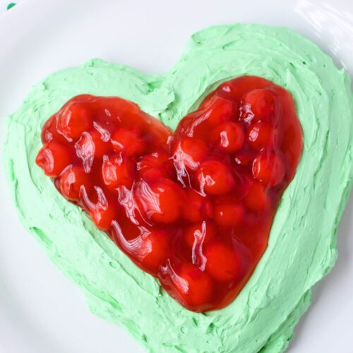 Festive Grinch dip with bright green cheesecake base and cherry topping shaped like a heart