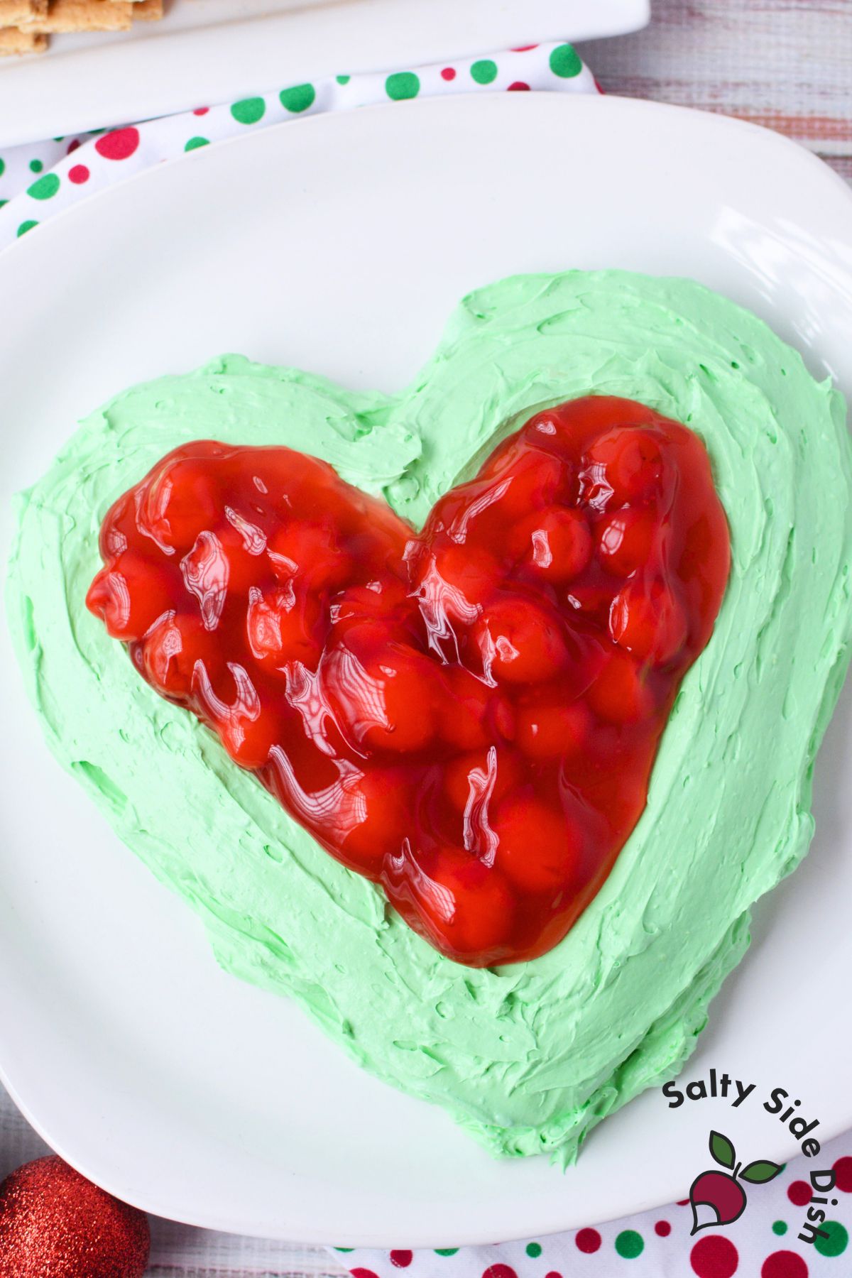 Festive Grinch dip with bright green cheesecake base and cherry topping shaped like a heart