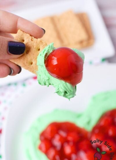 Festive Grinch dip with bright green cheesecake base and cherry topping shaped like a heart