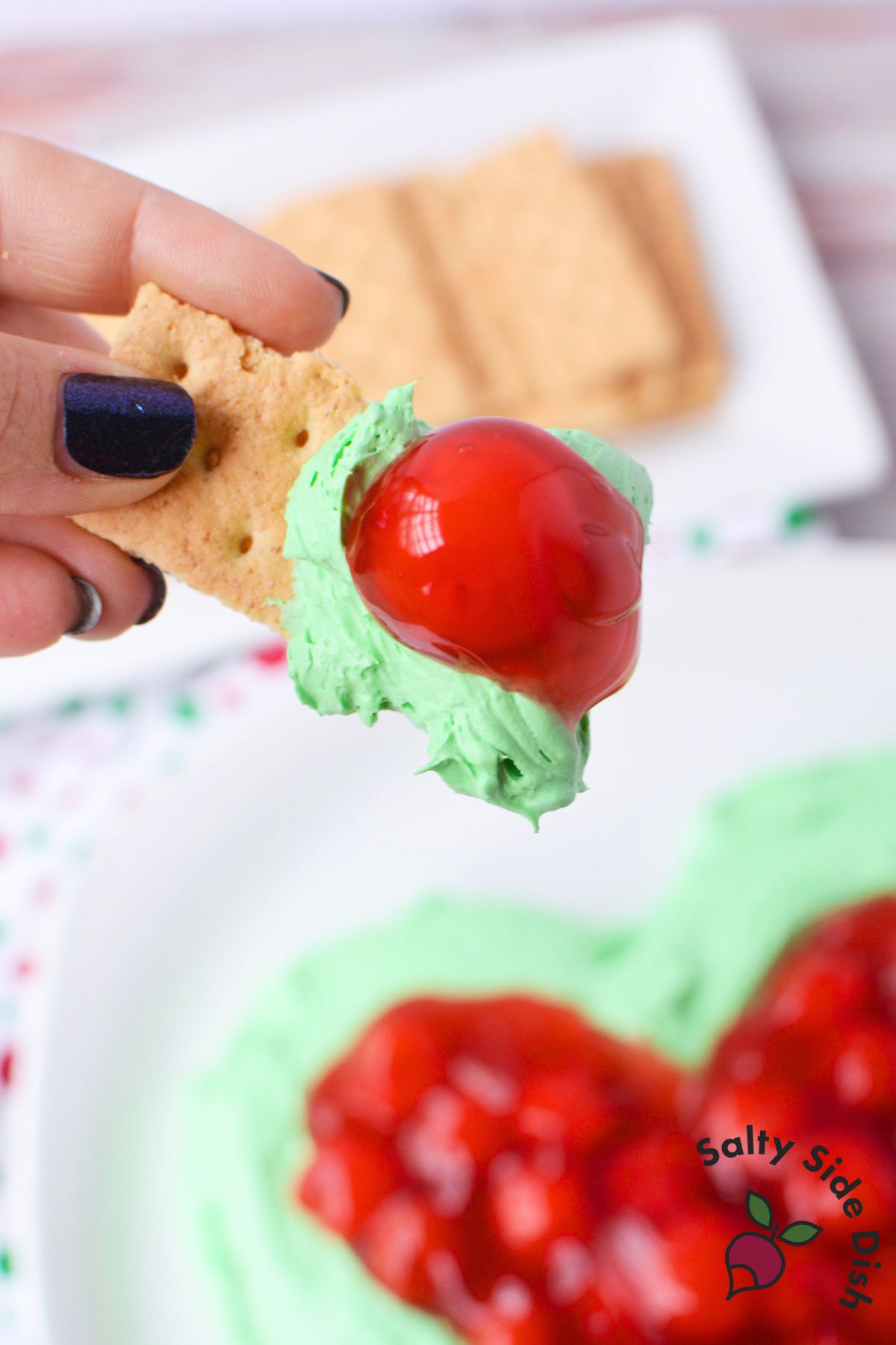 Festive Grinch dip with bright green cheesecake base and cherry topping shaped like a heart