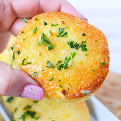 Hand holding a crispy round .garlic bread disk topped with fresh parsley