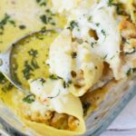 Spoonful of chicken Alfredo stuffed shells in a creamy garlic sauce, scooped from a baking dish with visible melted cheese and herbs.