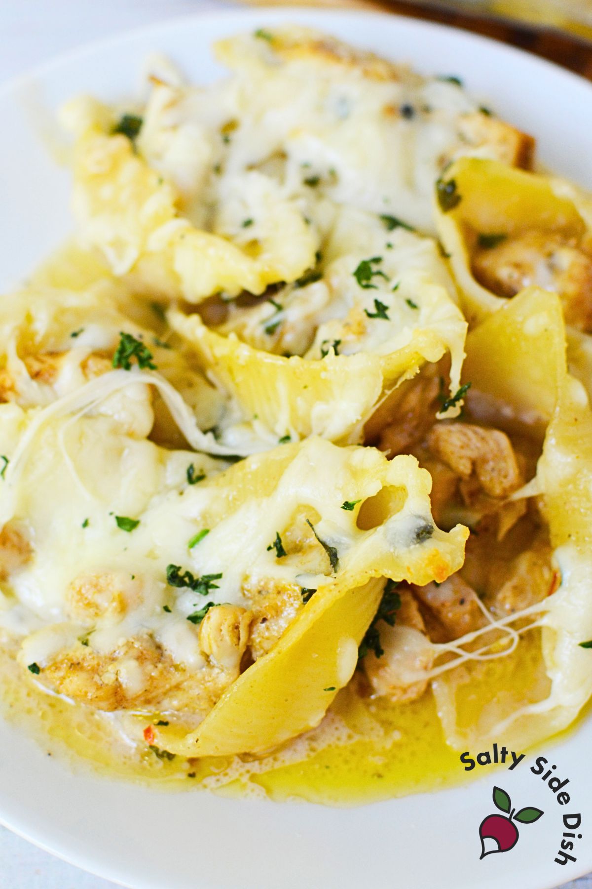 Spoonful of chicken Alfredo stuffed shells in a creamy garlic sauce, scooped from a baking dish with visible melted cheese and herbs.