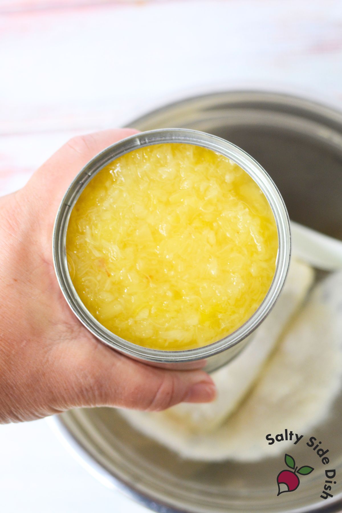 Hand holding open can of crushed pineapple, key ingredient for pineapple dip with cream cheese