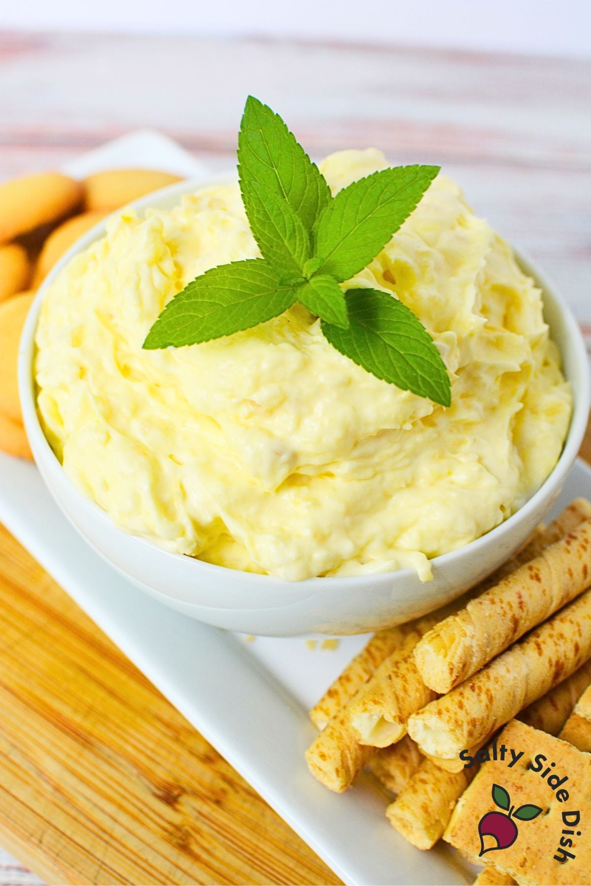 Creamy pineapple dip with cream cheese served in a white bowl with vanilla wafer sticks and fresh mint garnish
