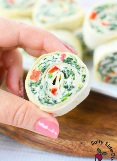 Close-up of hand holding a sliced spinach pinwheel appetizer with visible red pepper and spinach layers