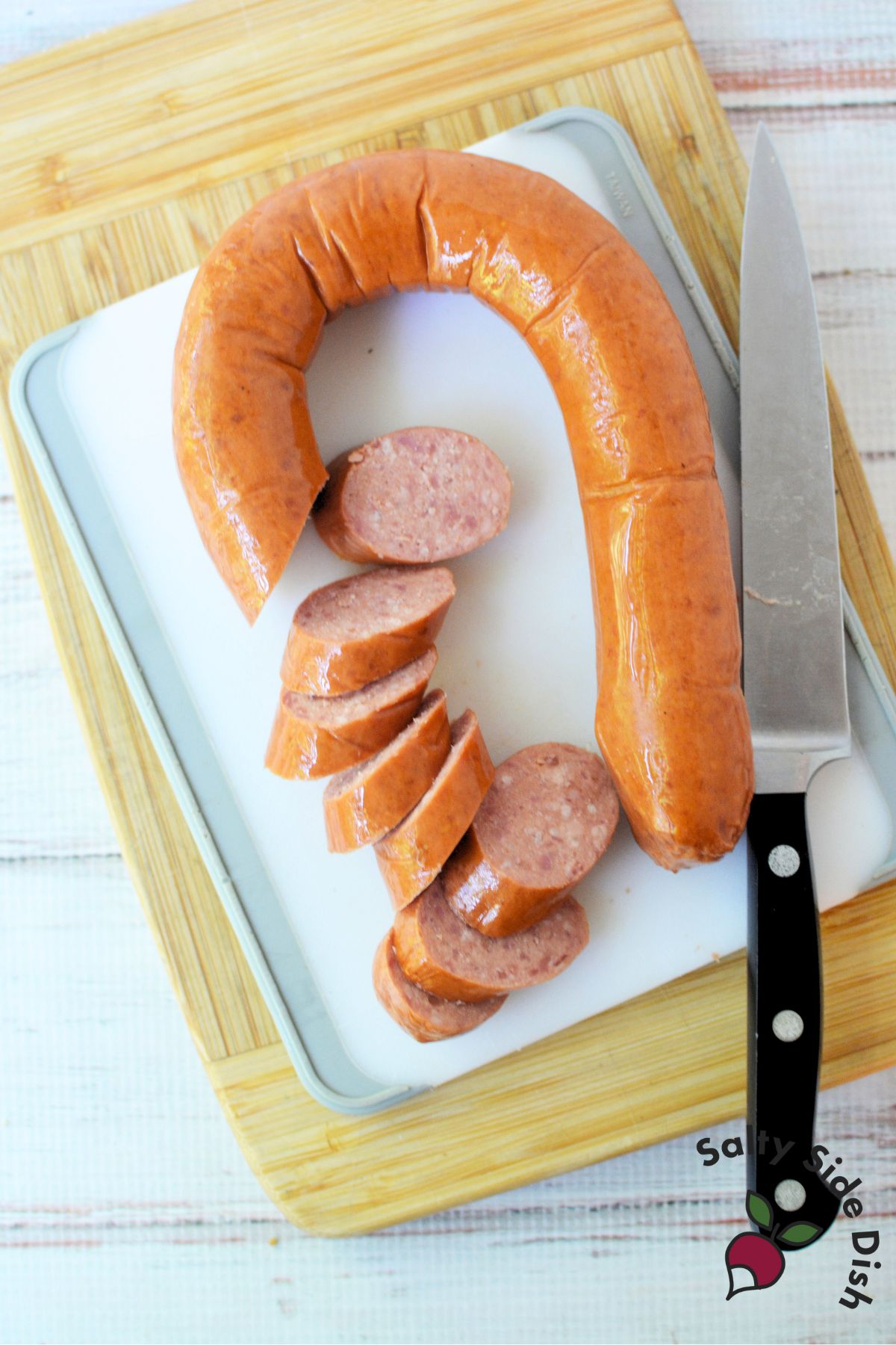 Conecuh smoked sausage sliced into rounds on white cutting board with chef’s knife