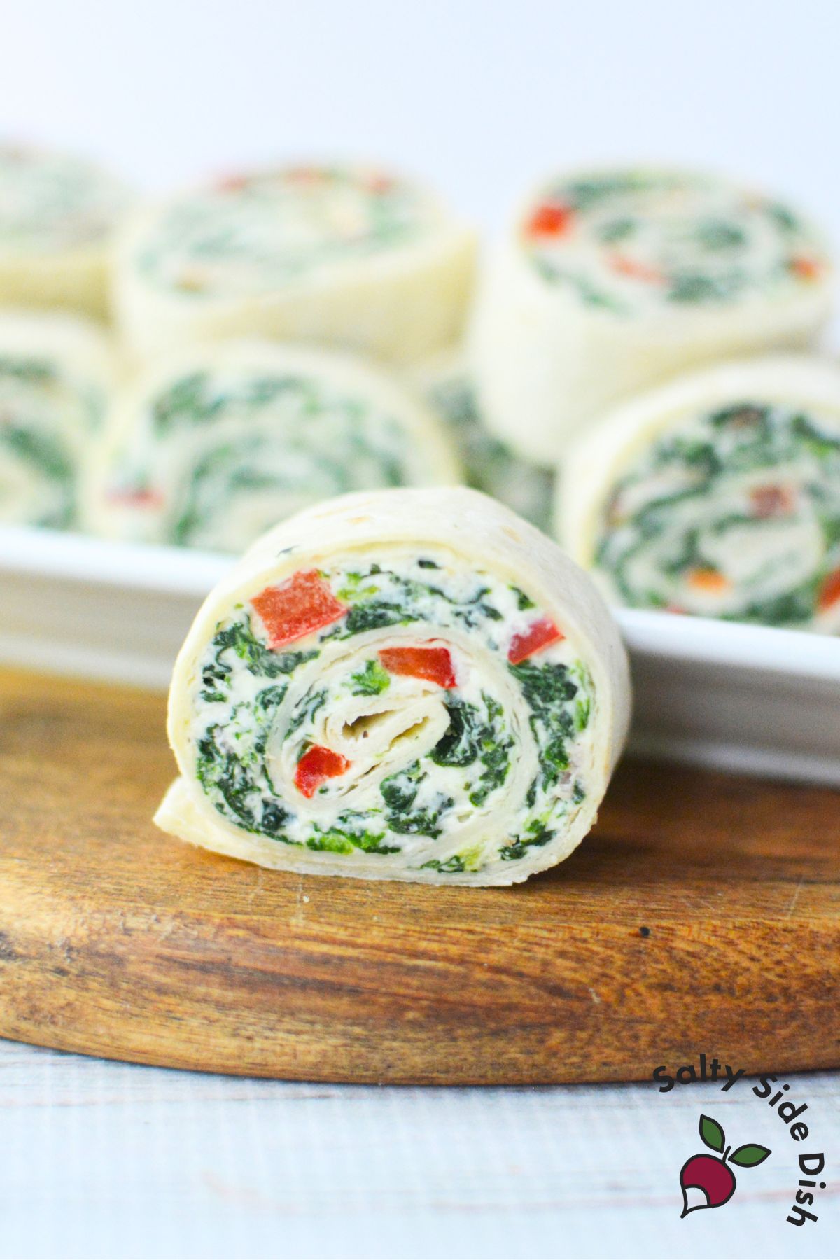 rolled up spinach dip pinwheel with platter behind it.