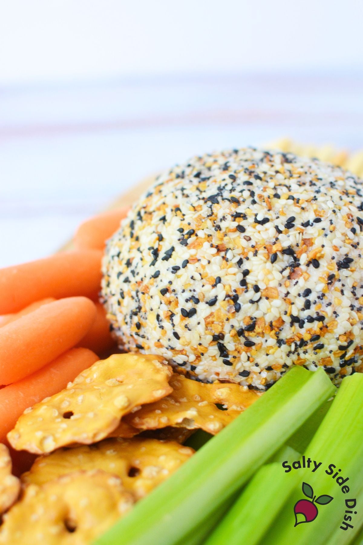 Close-up of everything bagel cheese ball surrounded by carrots, celery, and pretzels