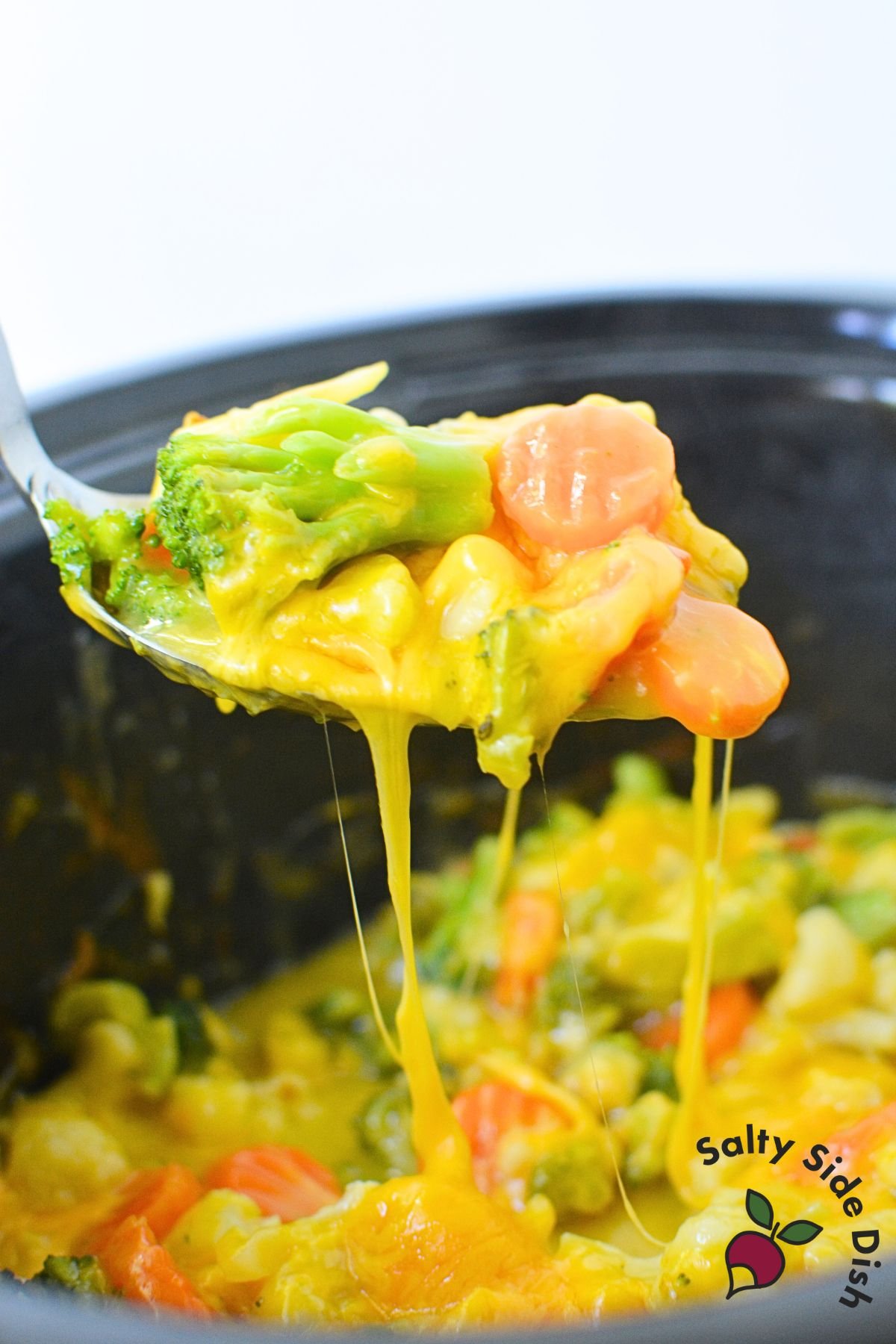 Frozen California medley vegetables (broccoli, carrots, cauliflower) in a spoon.