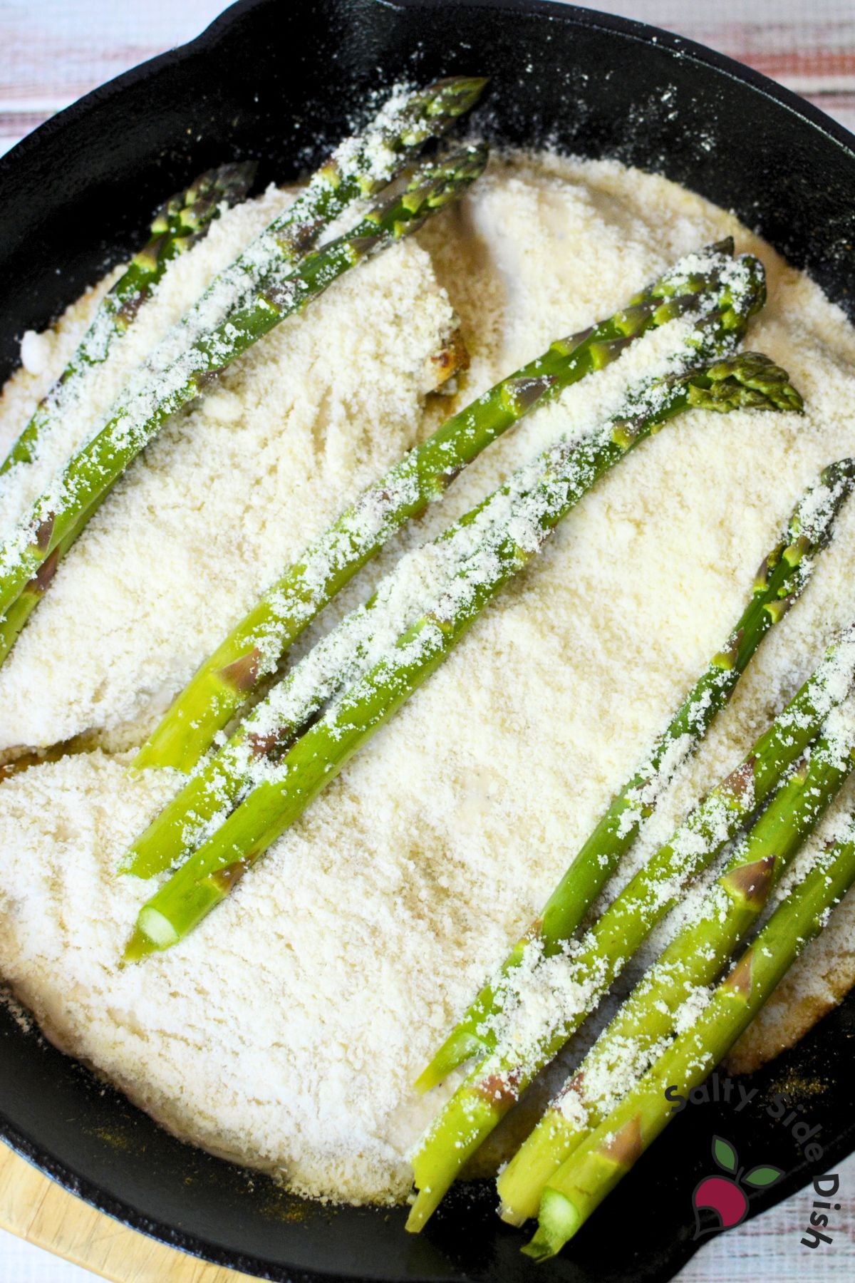 Cast iron skillet filled with Caesar chicken breasts and fresh asparagus spears