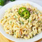 Mixing bowl with elbow macaroni, shredded cheddar cheese, crumbled bacon, and diced jalapenos for jalapeno popper pasta salad