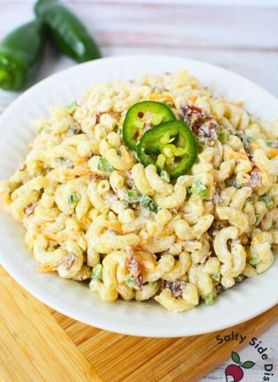 Mixing bowl with elbow macaroni, shredded cheddar cheese, crumbled bacon, and diced jalapenos for jalapeno popper pasta salad