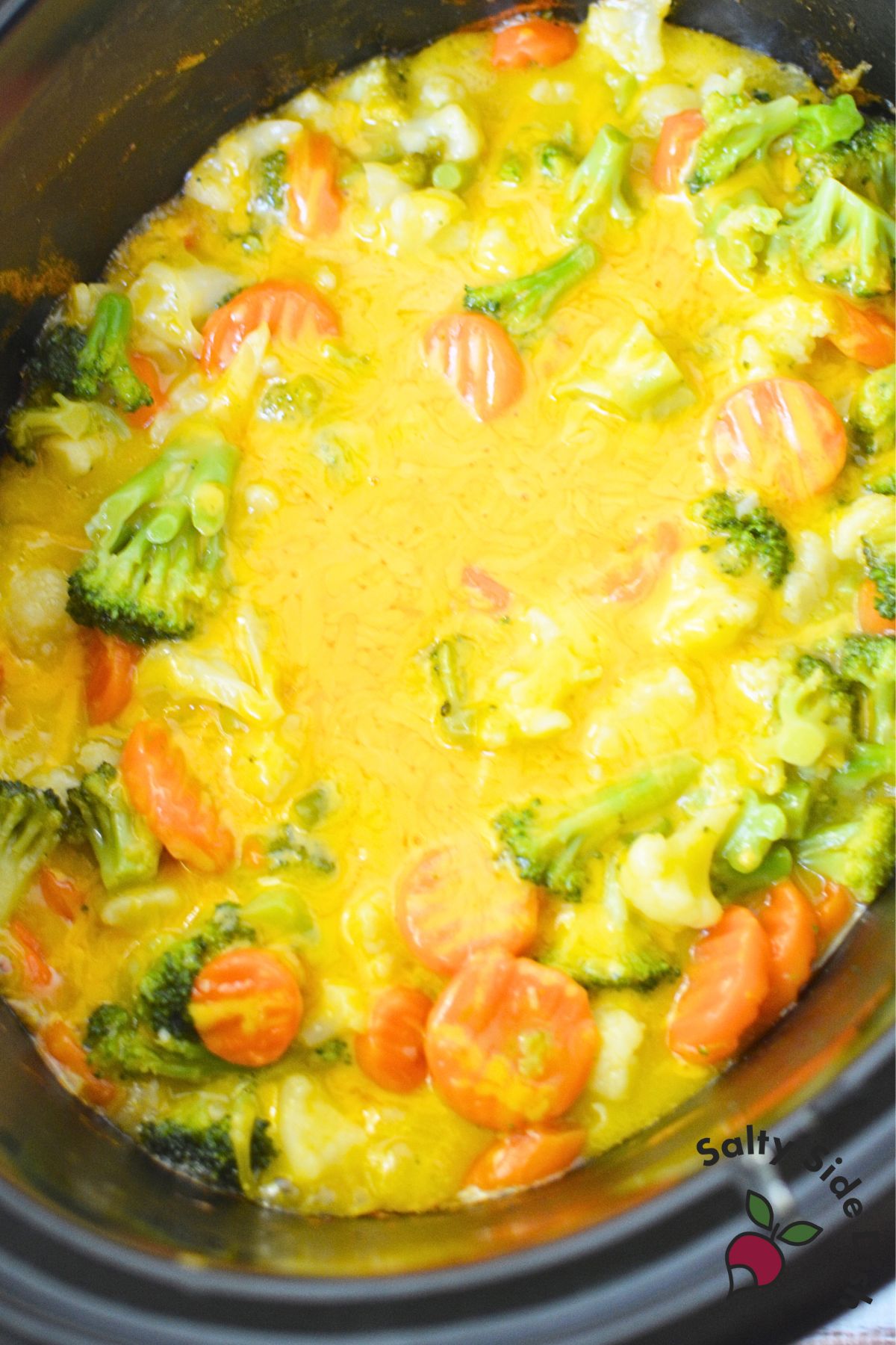 Cheddar cheese melting over vegetables in slow cooker