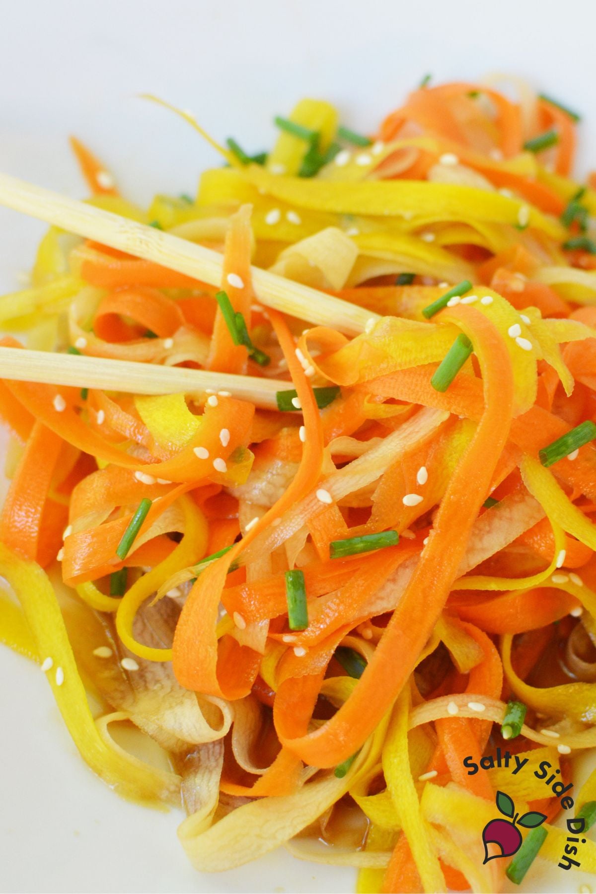 Viral TikTok carrot salad made with rainbow carrot ribbons lifted by chopsticks and topped with sesame seed