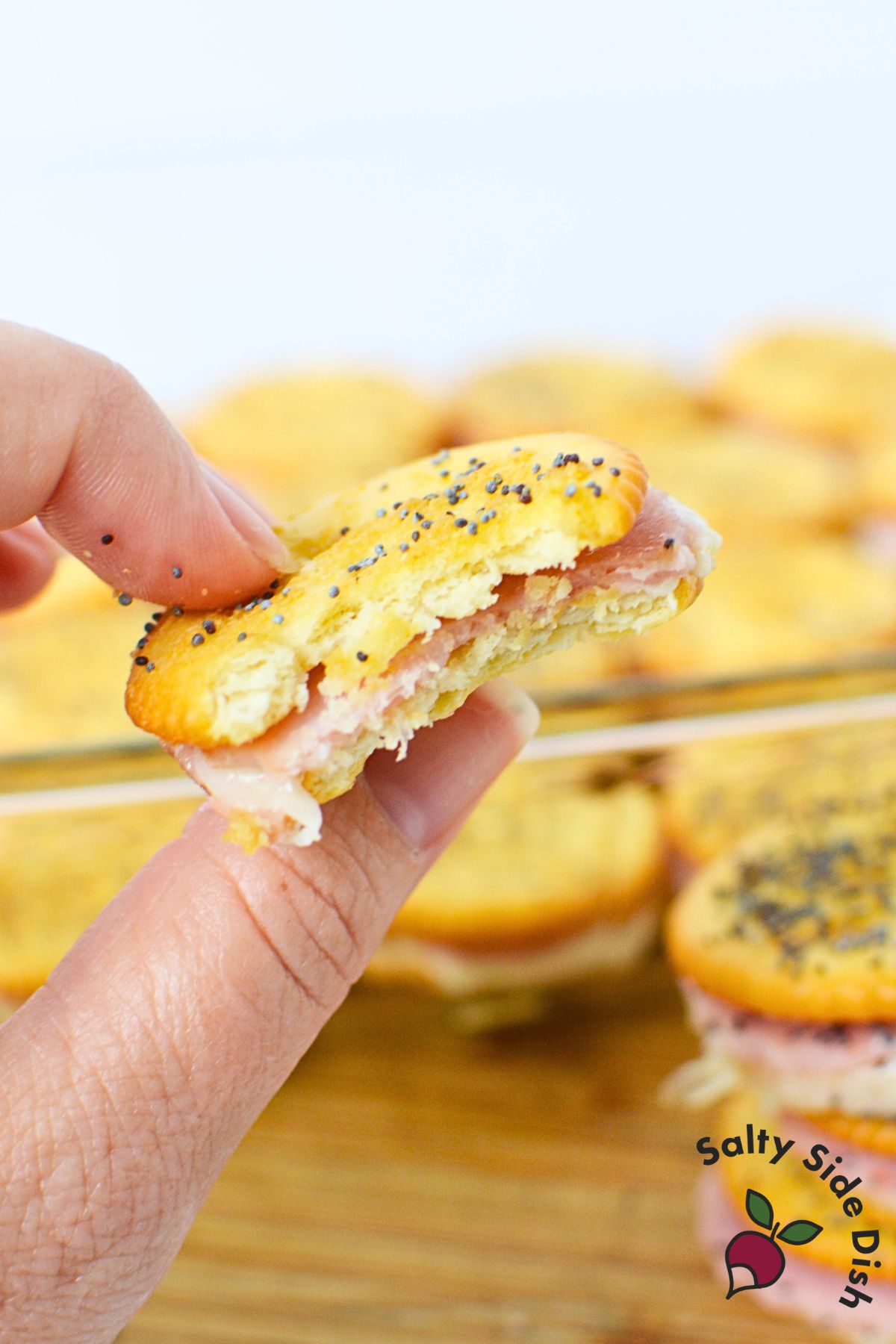 Close-up of a hand holding a bitten Ritz cracker sandwich with gooey cheese inside.