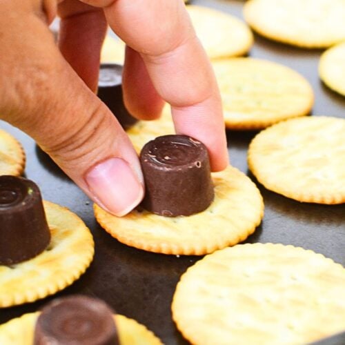 Hand placing a Rolo candy on top of Ritz cracker before baking