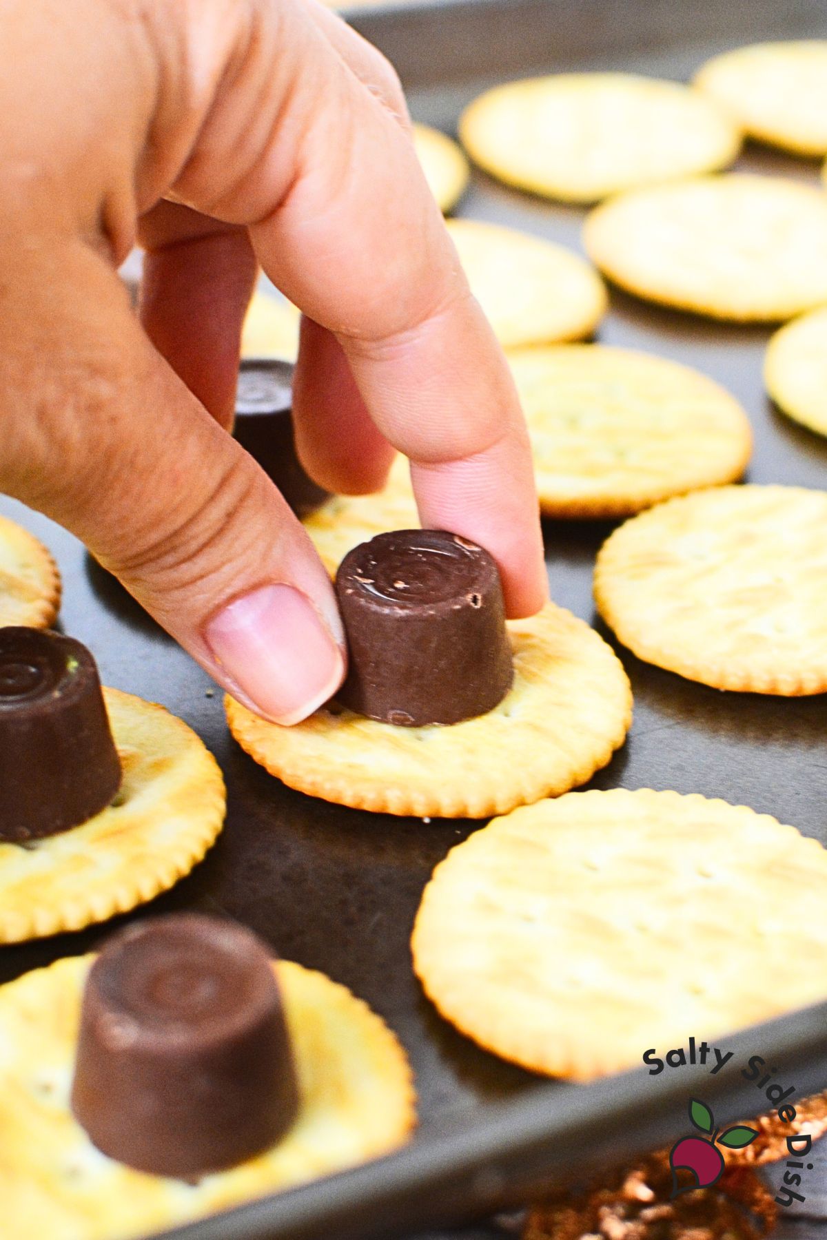 Hand placing a Rolo candy on top of Ritz cracker before baking